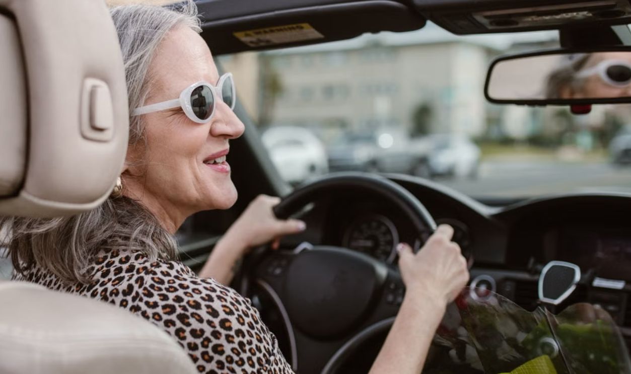 Senior woman driving a convertible, smiling and wearing sunglasses on a sunny day