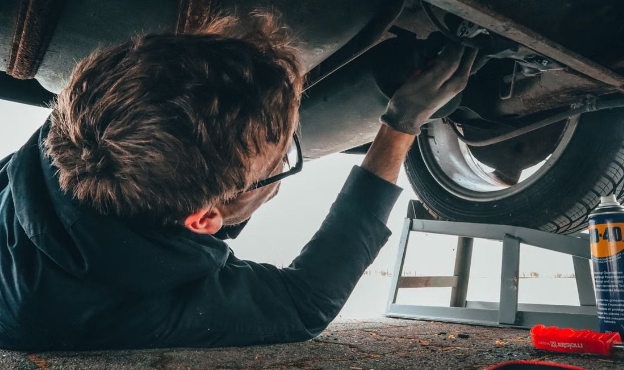 Mechanic skillfully repairing car undercarriage in outdoor setting with tools