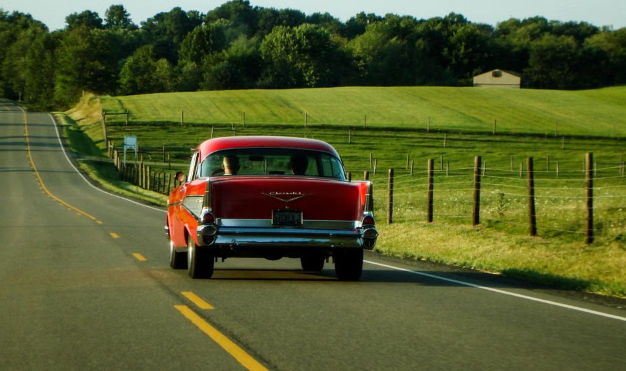 Classic red car driving on a scenic countryside road in Ohio, capturing a vintage travel vibe
