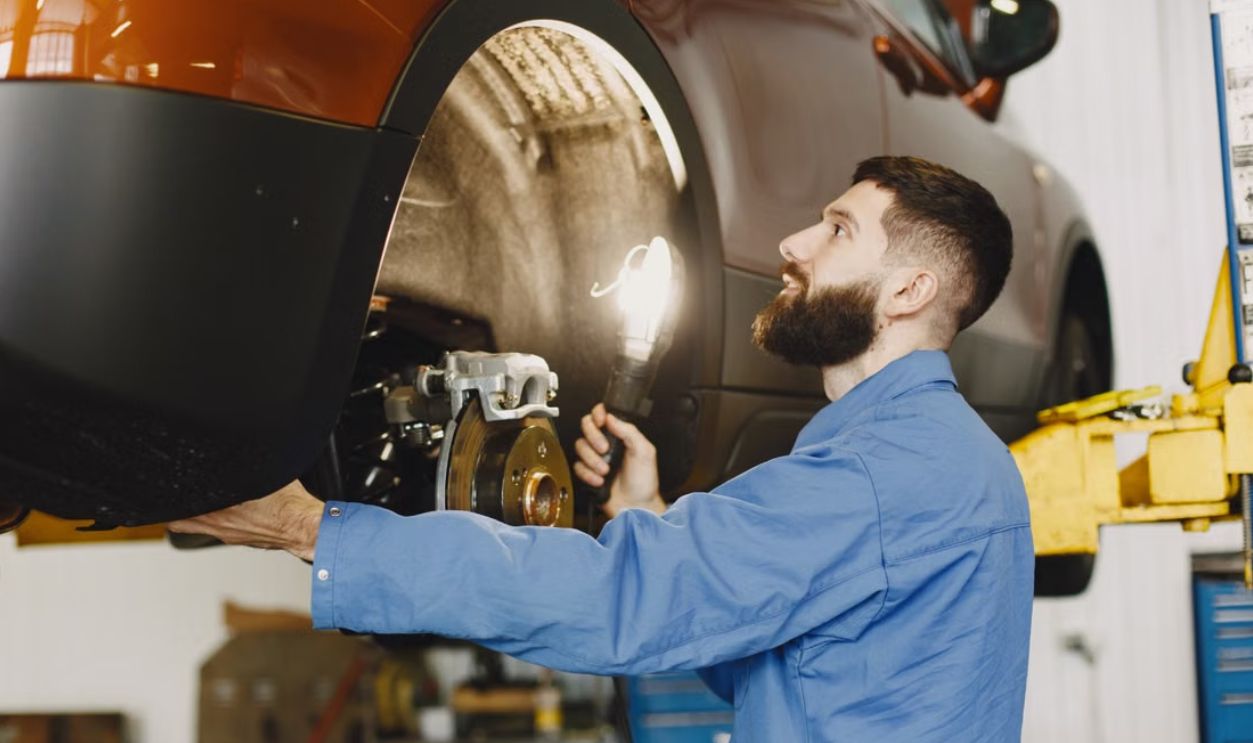 Professional mechanic in blue coveralls inspecting car brakes in a well-lit garage