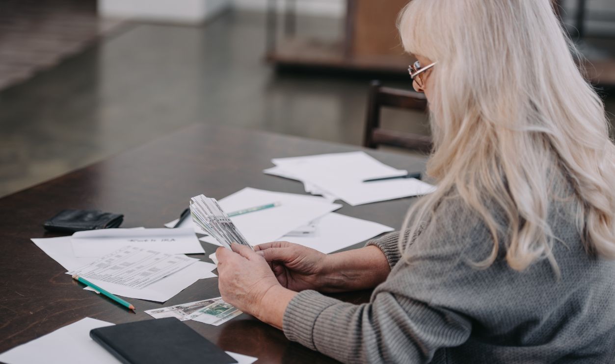 senior woman sitting at table with paperwork and counting money