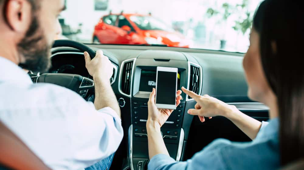 Back view of young Lover couple in car, man driving in city and woman using navigation on mobile phone or some apps