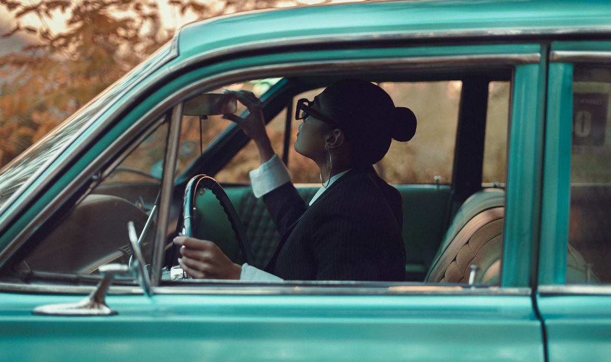Woman in vintage car adjusting mirror, exuding elegance