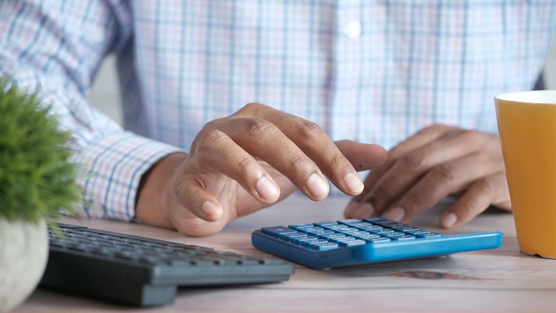 person using calculator at desk with coffee mug