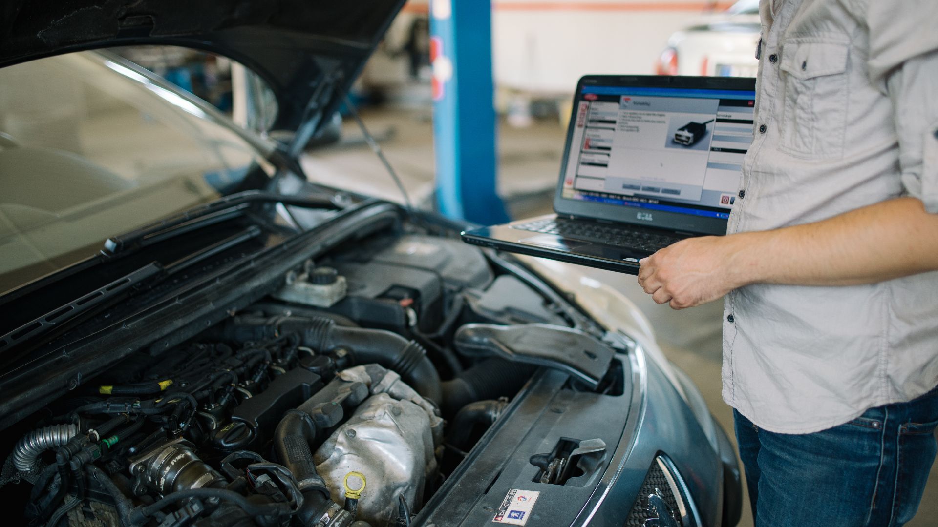 Young mechanic with modern laptop doing car diagnostic at automobile repair