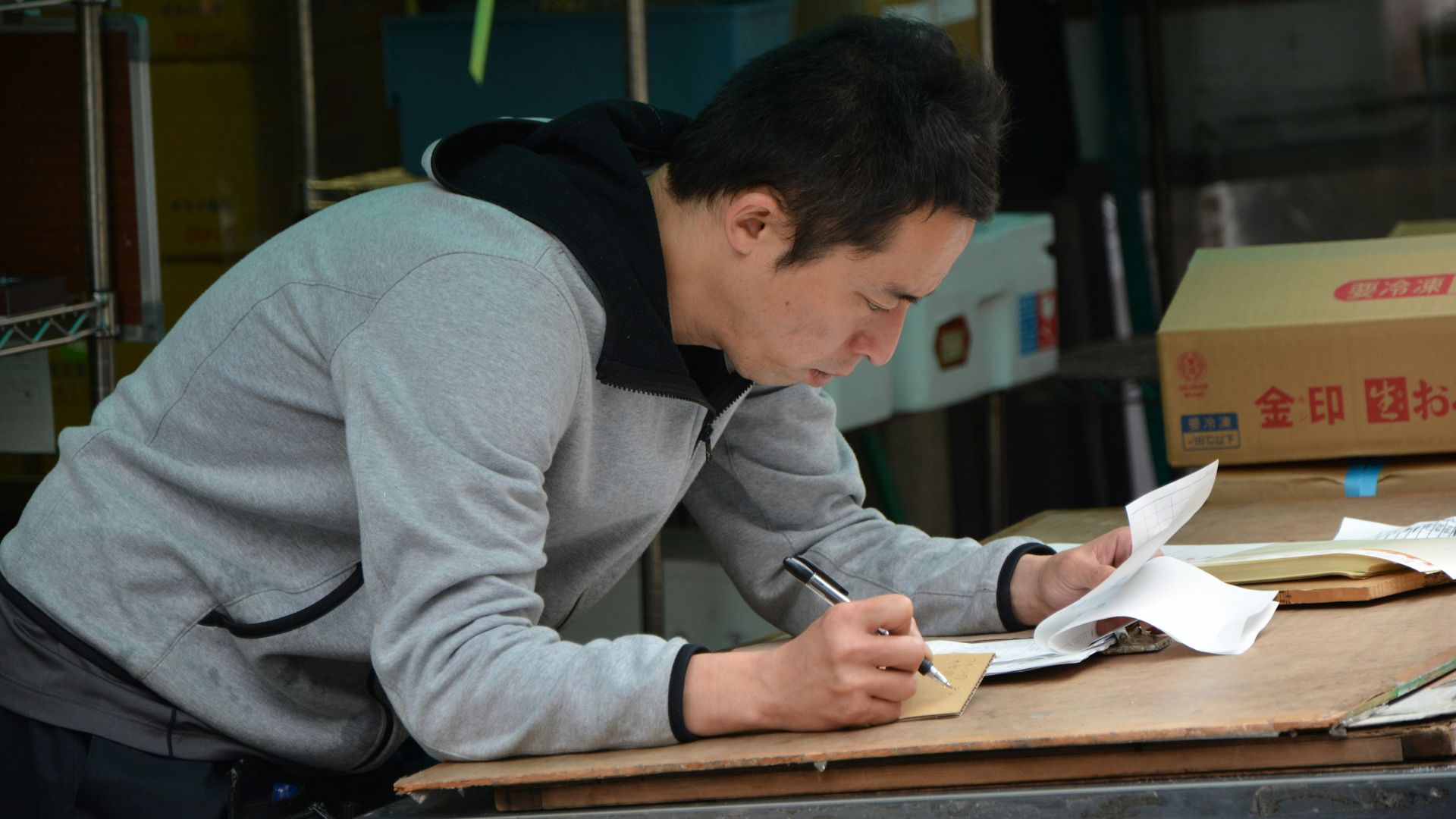 man in gray hoodie writing on white paper