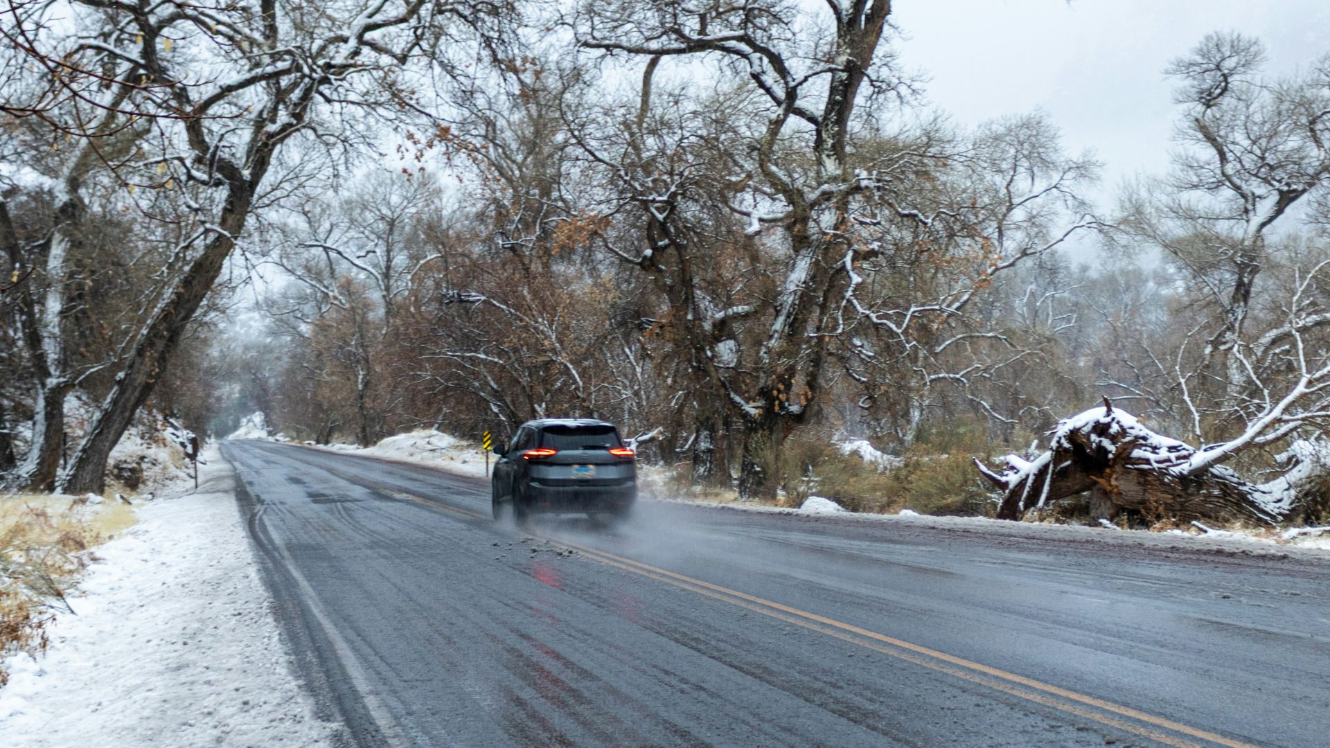 A car drives on a wet road in snowy weather.