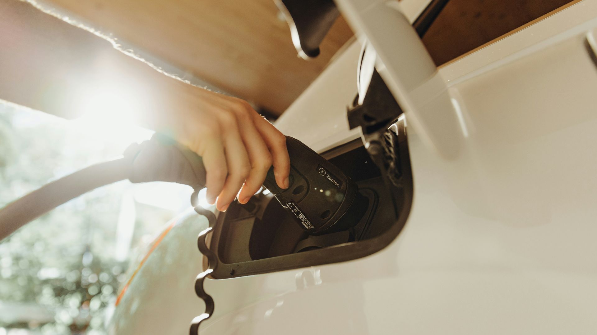 A hand plugging a charging cable into a white electric vehicle
