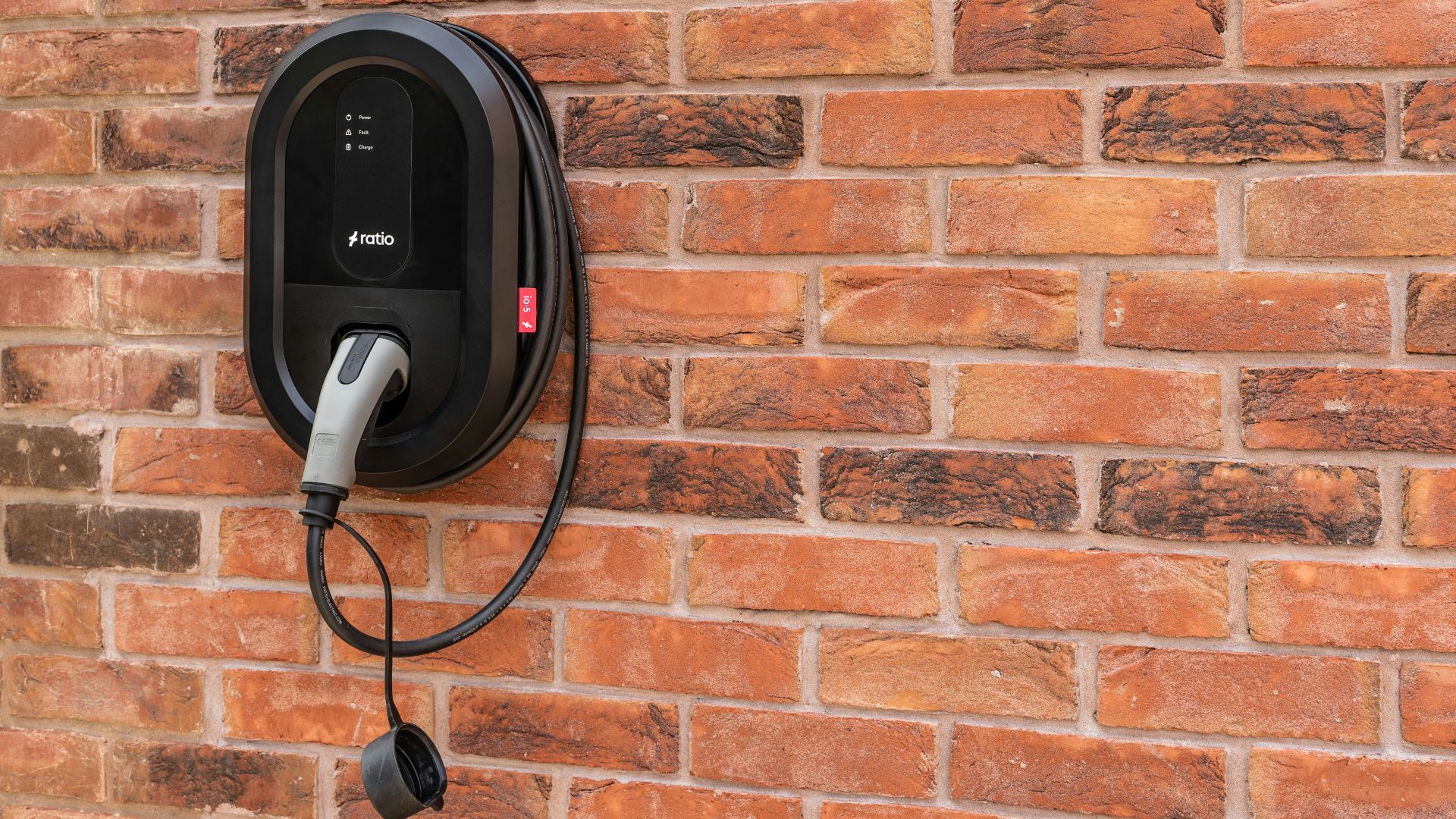 Black electric car charger mounted on brick wall
