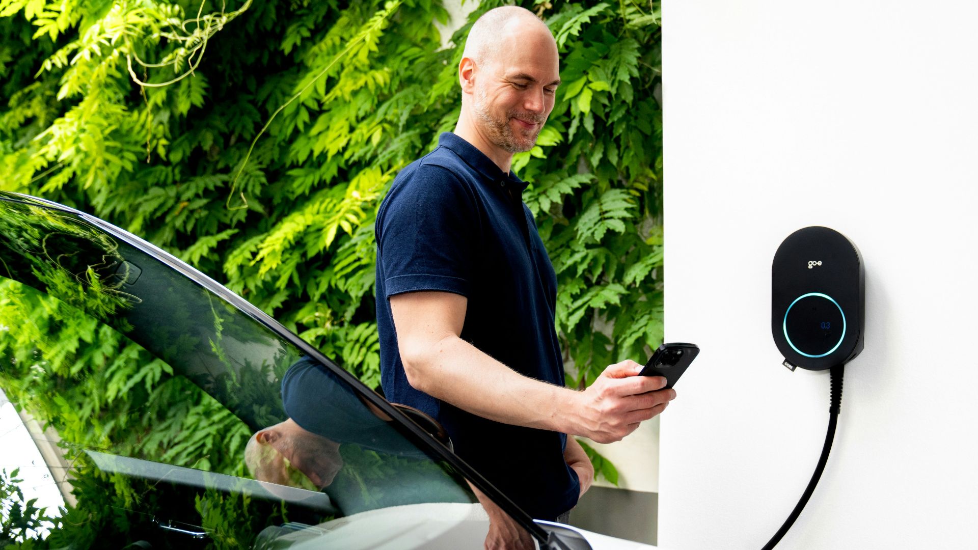 Man using phone near electric car charging station