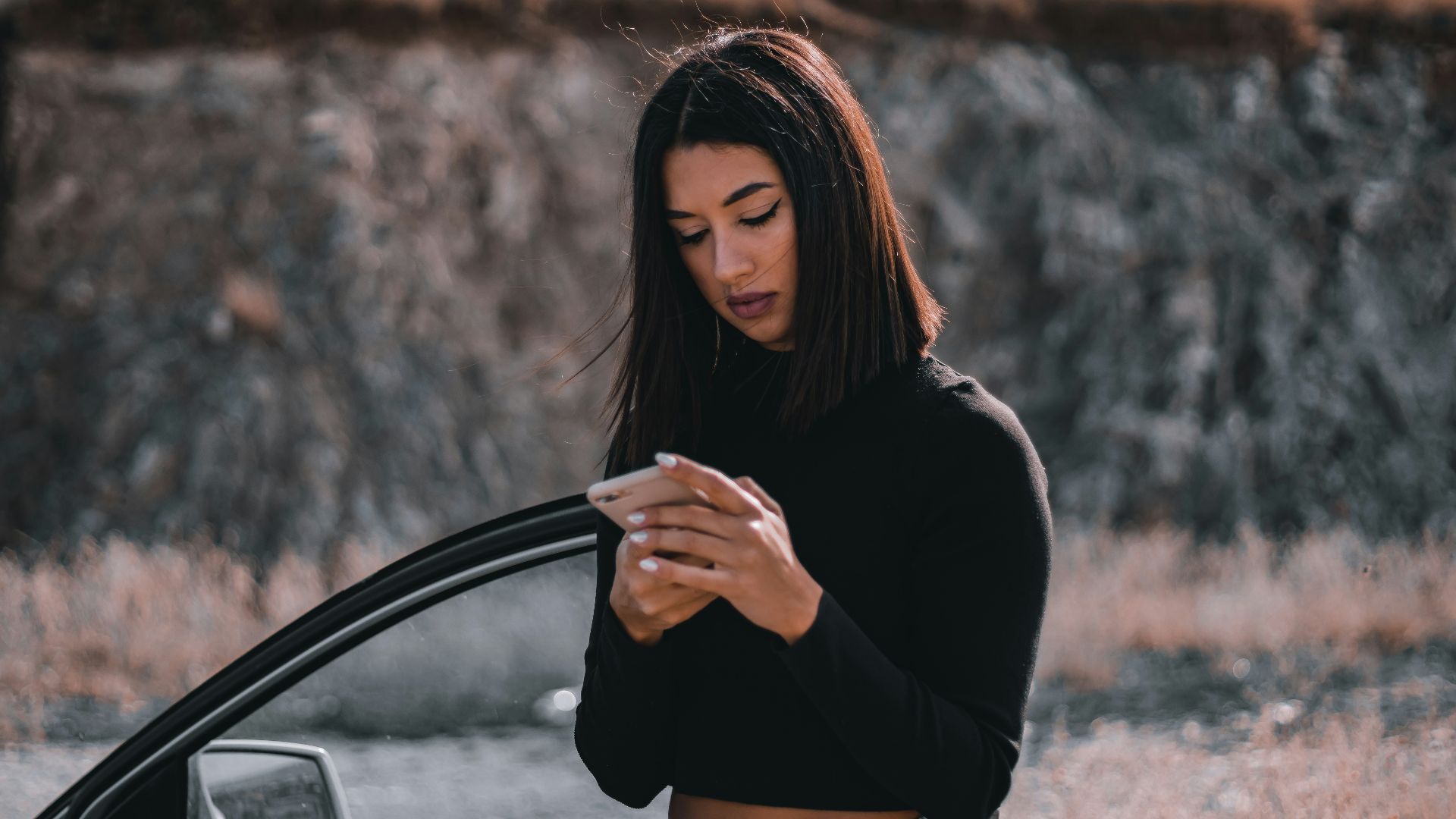 a woman standing next to a car looking at her cell phone