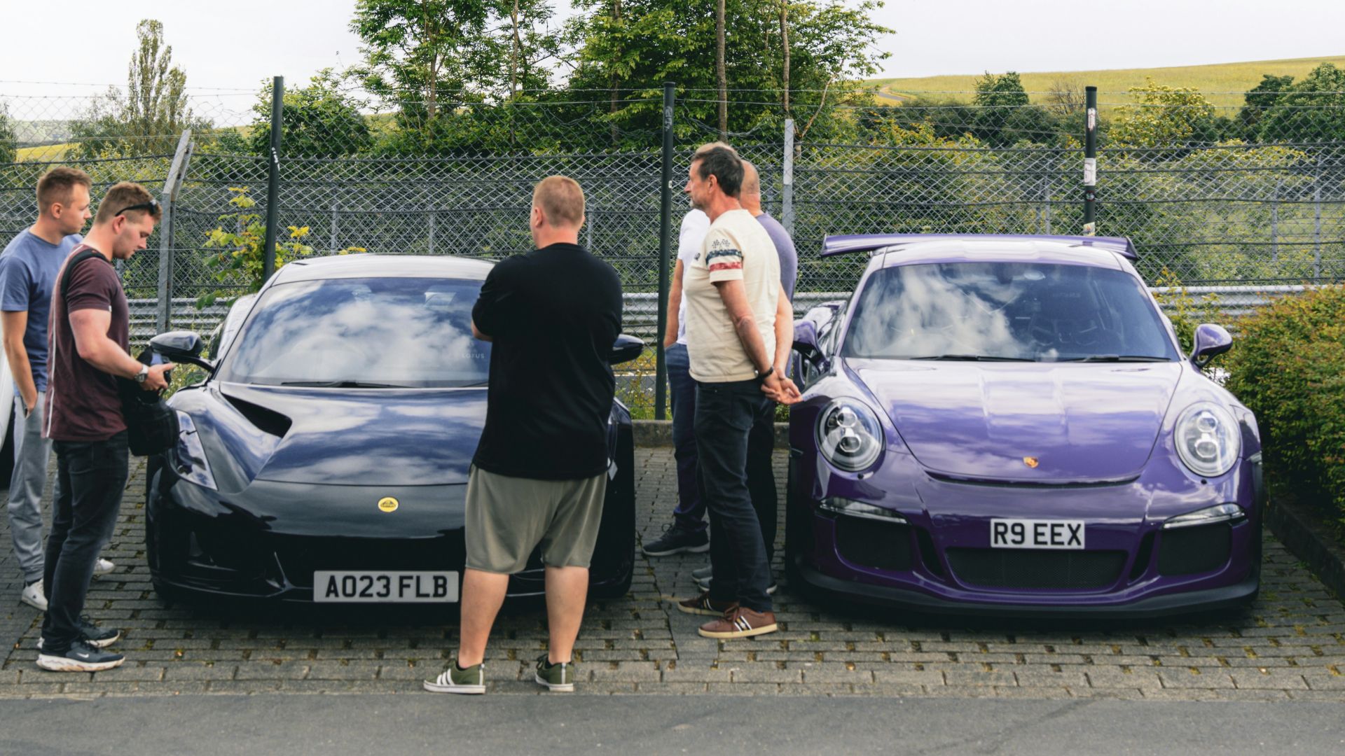 A group of people standing next to a row of parked cars