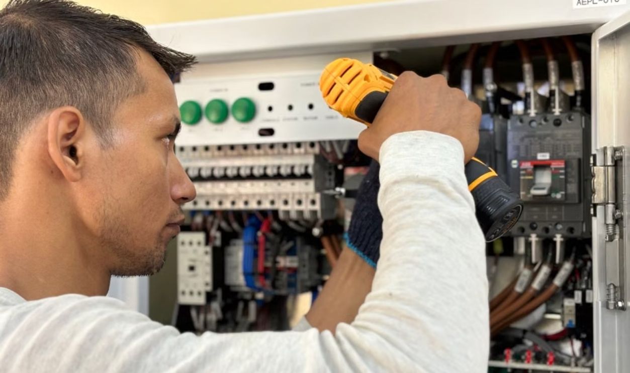Professional electrician using a drill on an indoor circuit breaker panel.