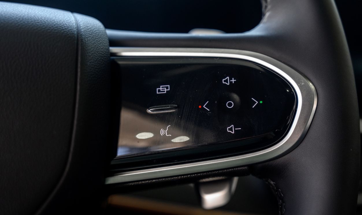 A close-up of a modern car's steering wheel, made of smooth black leather with silver accents and control buttons