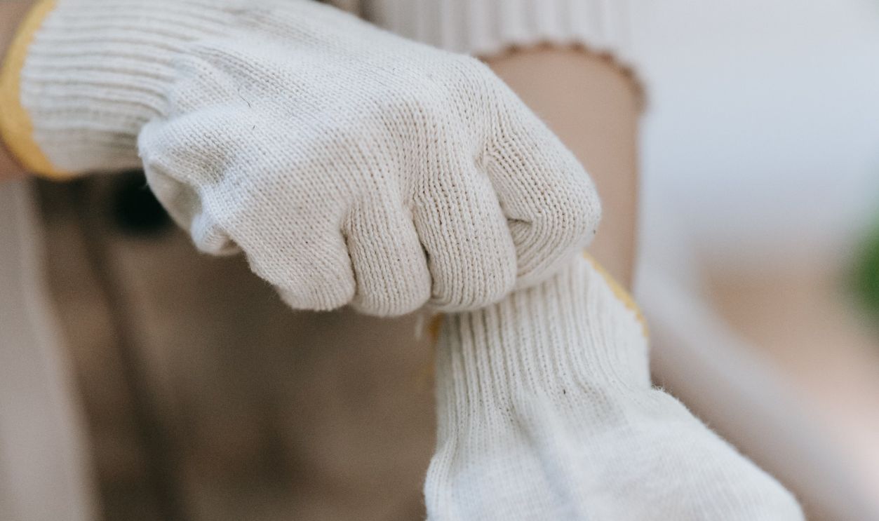 A detailed shot of hands putting on white knitted gloves indoors. Ideal for gardening themes