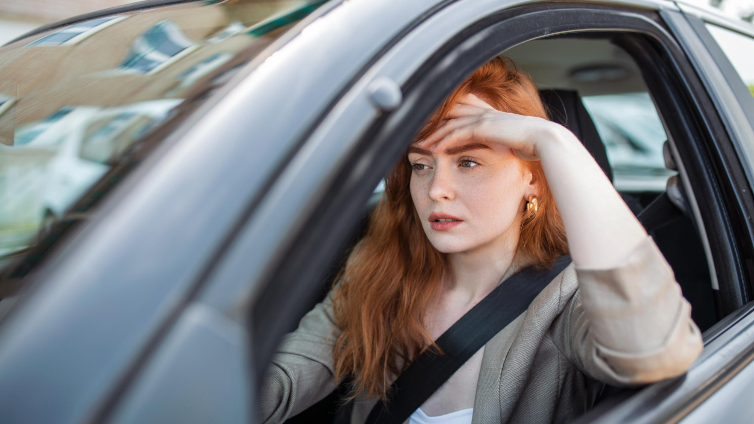 Sad young woman is seating inside a car and thinking.