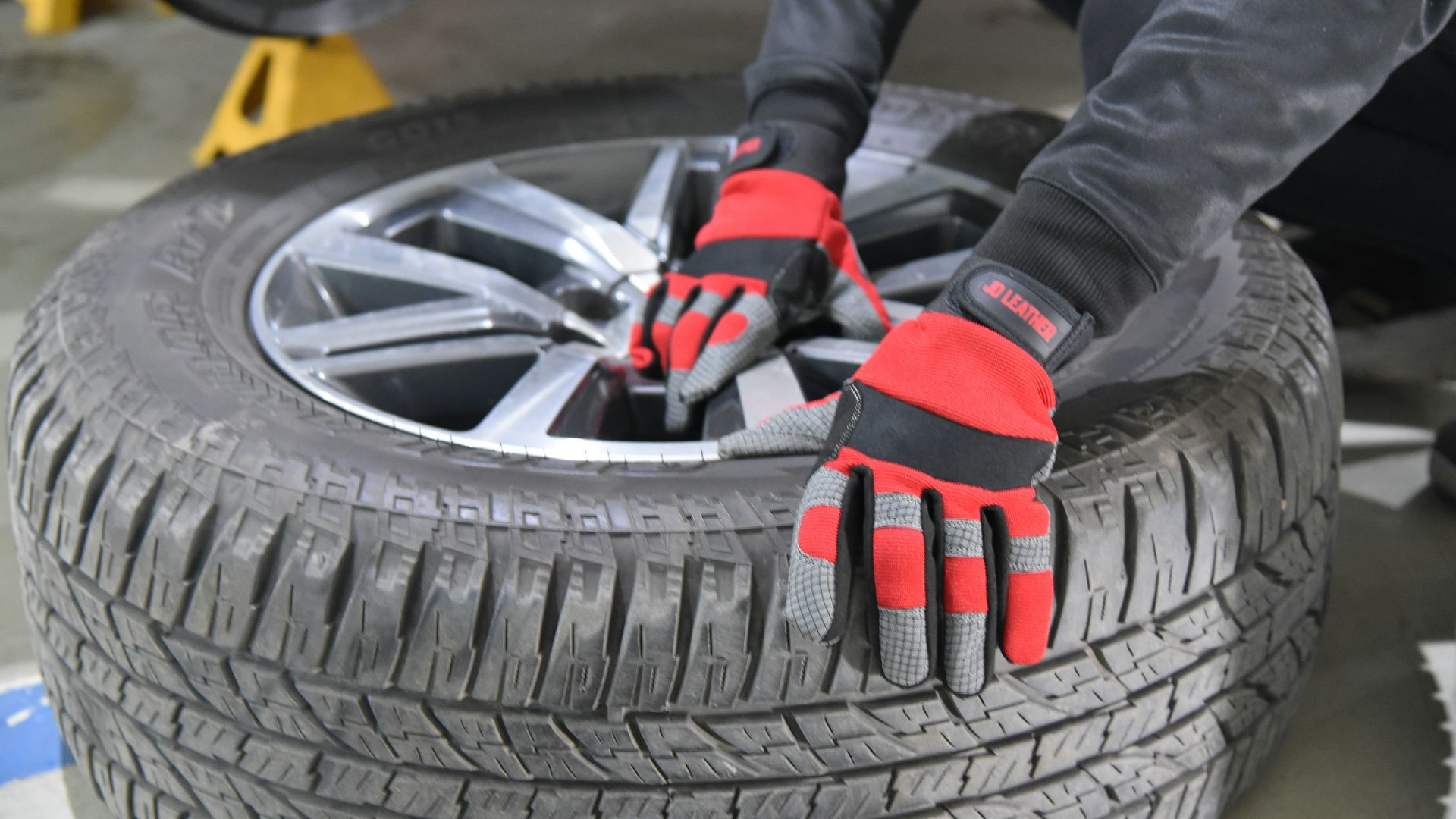 A person wearing red gloves works on a car tire