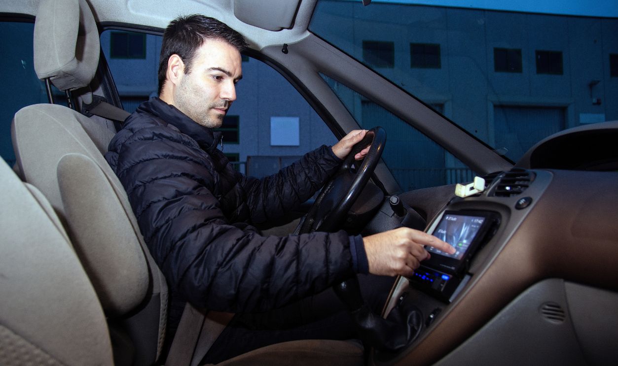 Shutterstock-2754469759, Man using touchscreen display in car while driving