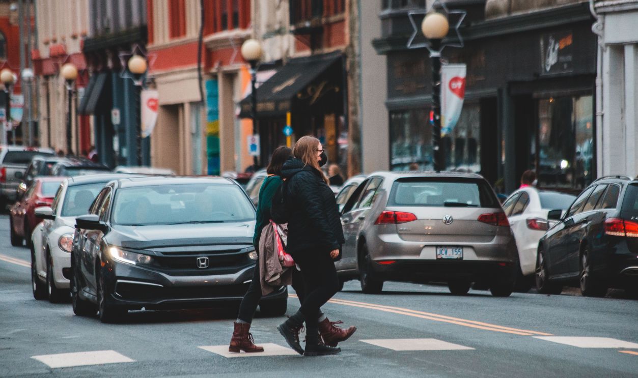 Pedestrians wearing winter clothes cross a busy urban street with traffic and historic buildings