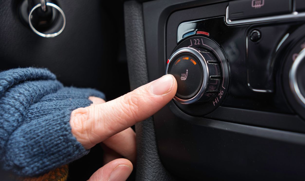 Driver in warm glove presses seat heating button to quickly add warmth inside car during a cold winter ride