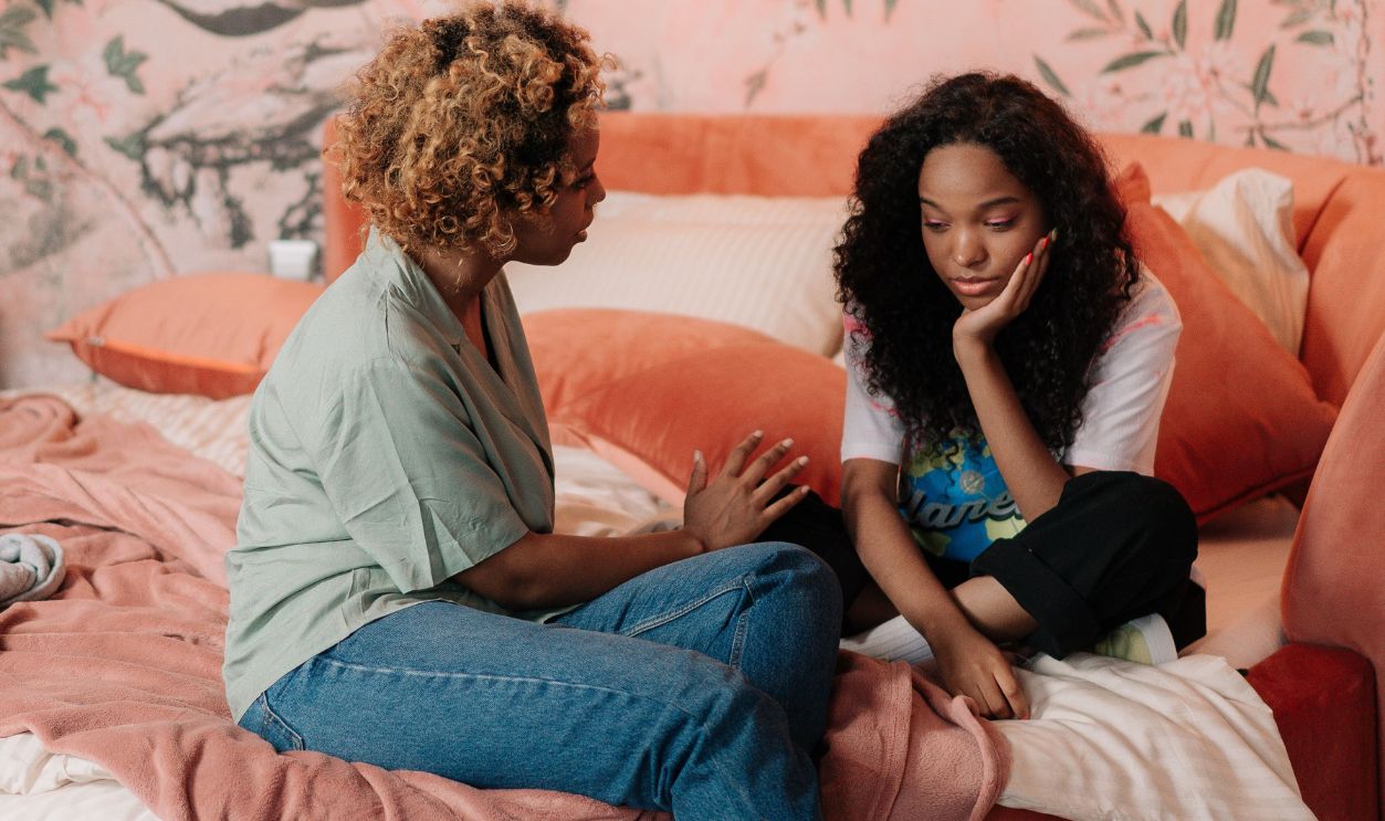 A mother and daughter sharing a bonding moment on a cozy bed with artistic wall decor.
