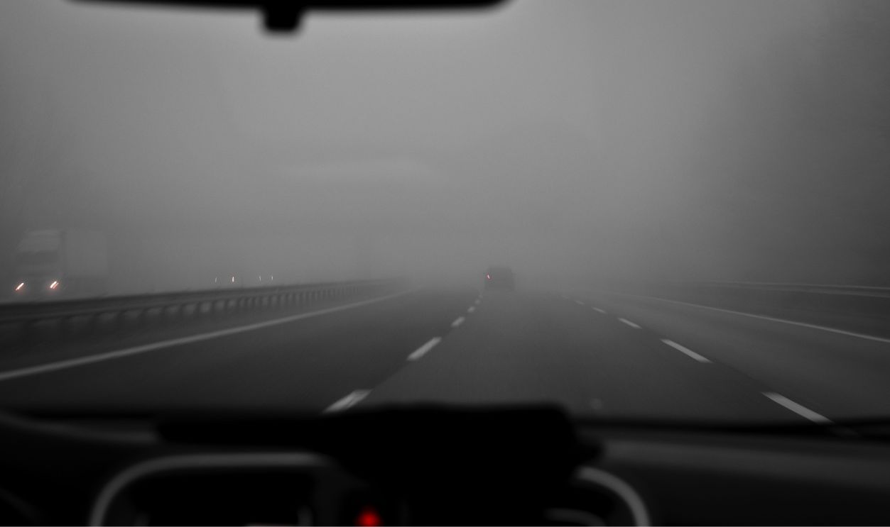 Car interior view of a foggy highway creating a mysterious, overcast atmosphere.