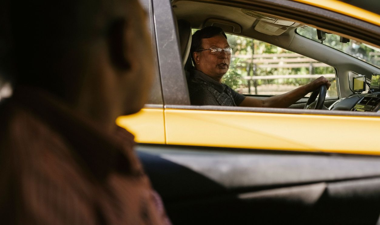 Two taxi drivers caught in conversation at an urban intersection, highlighting diverse urban lifestyles