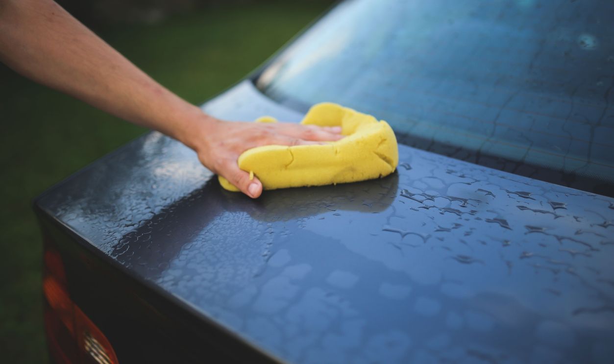Hand cleaning car with a yellow sponge, showcasing car detailing and washing