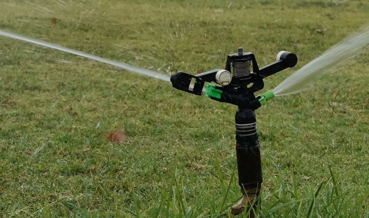 Rotating sprinkler watering a lush green lawn on an overcast day.