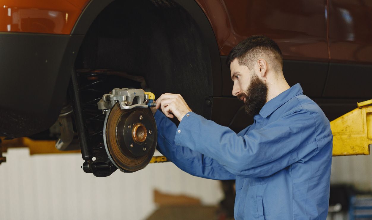 Mechanic in blue uniform performing brake repair on car
