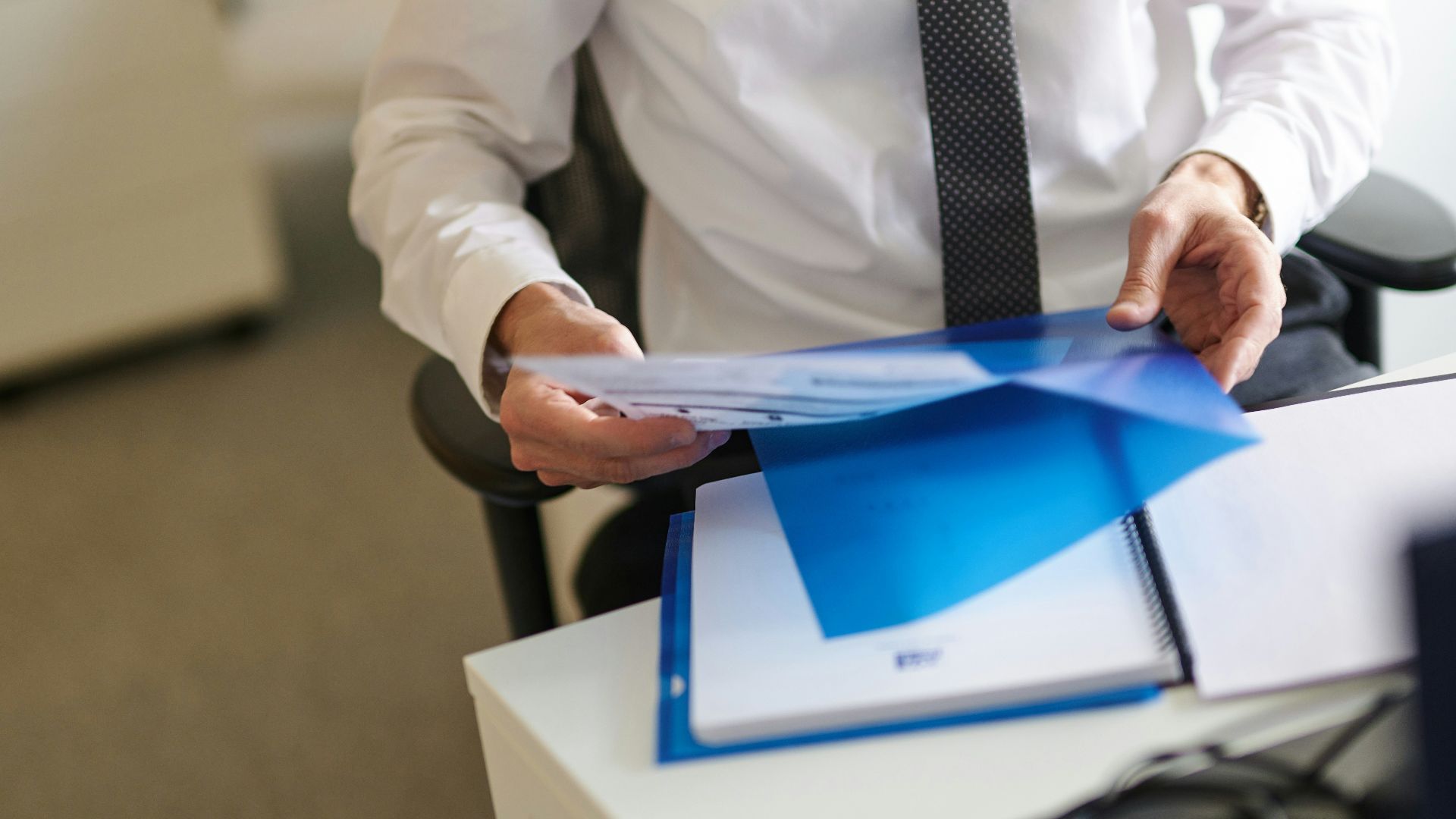 a man in a white shirt and tie holding a folder