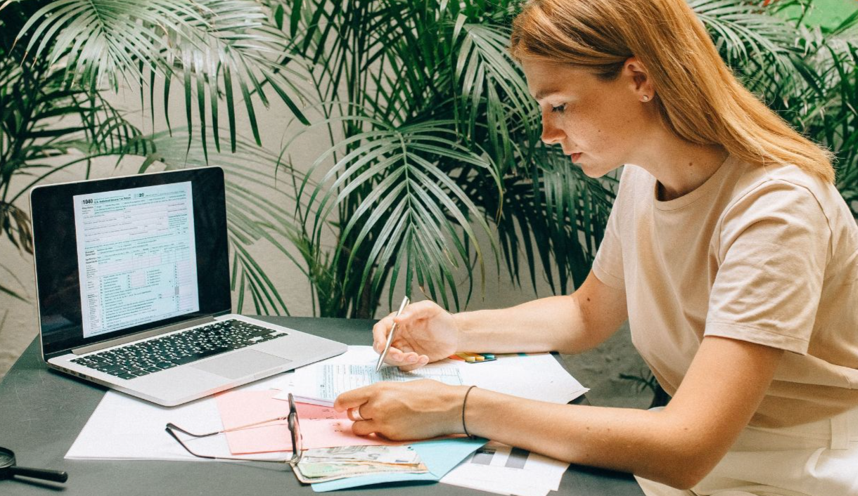 A woman deeply concentrated on work at her laptop amidst indoor greenery and documents