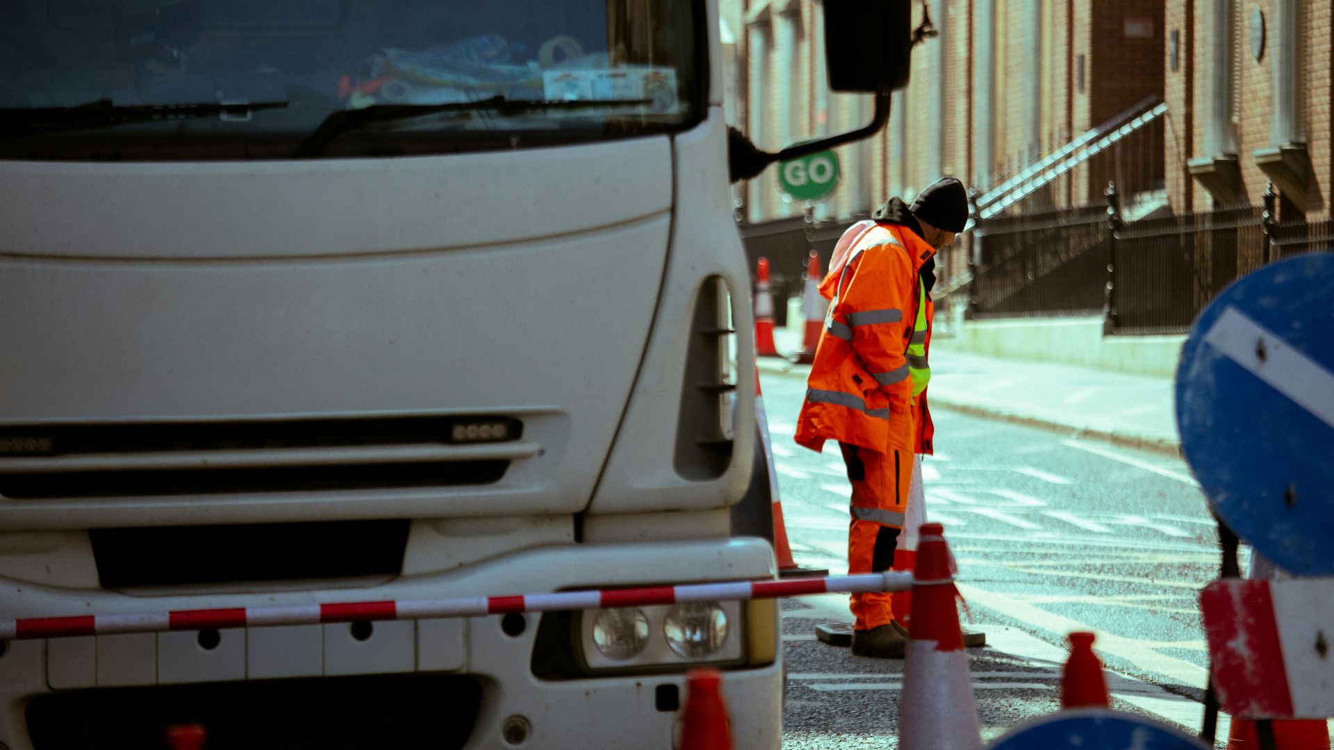 Worker in orange vest near truck and traffic cones