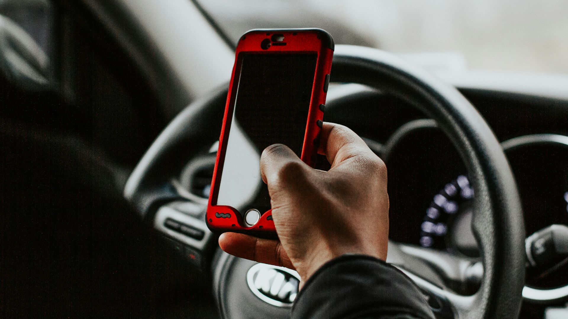 person holding red smartphone sitting in front of vehicle steering wheel