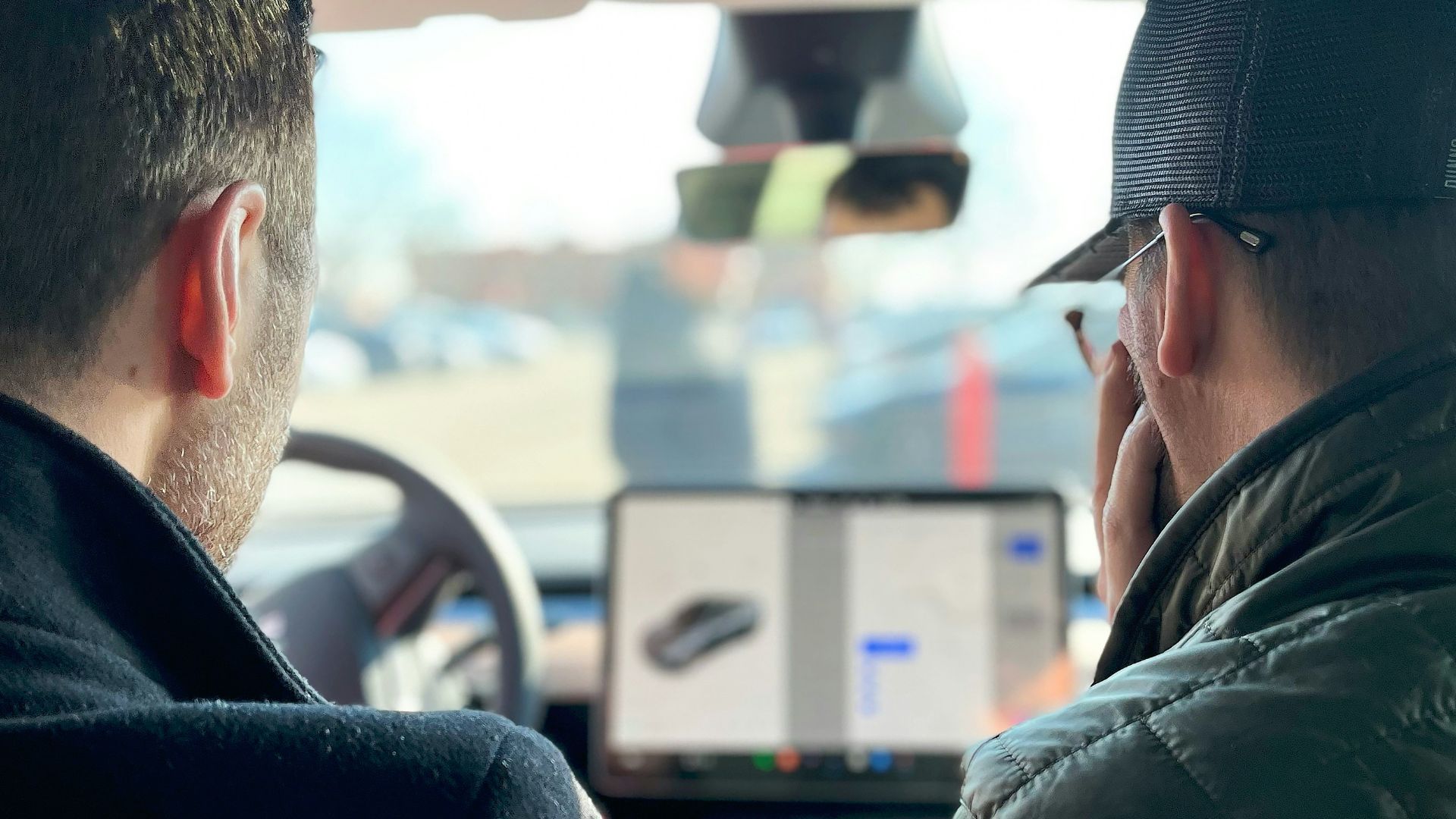 two men sitting in a car talking on their cell phones