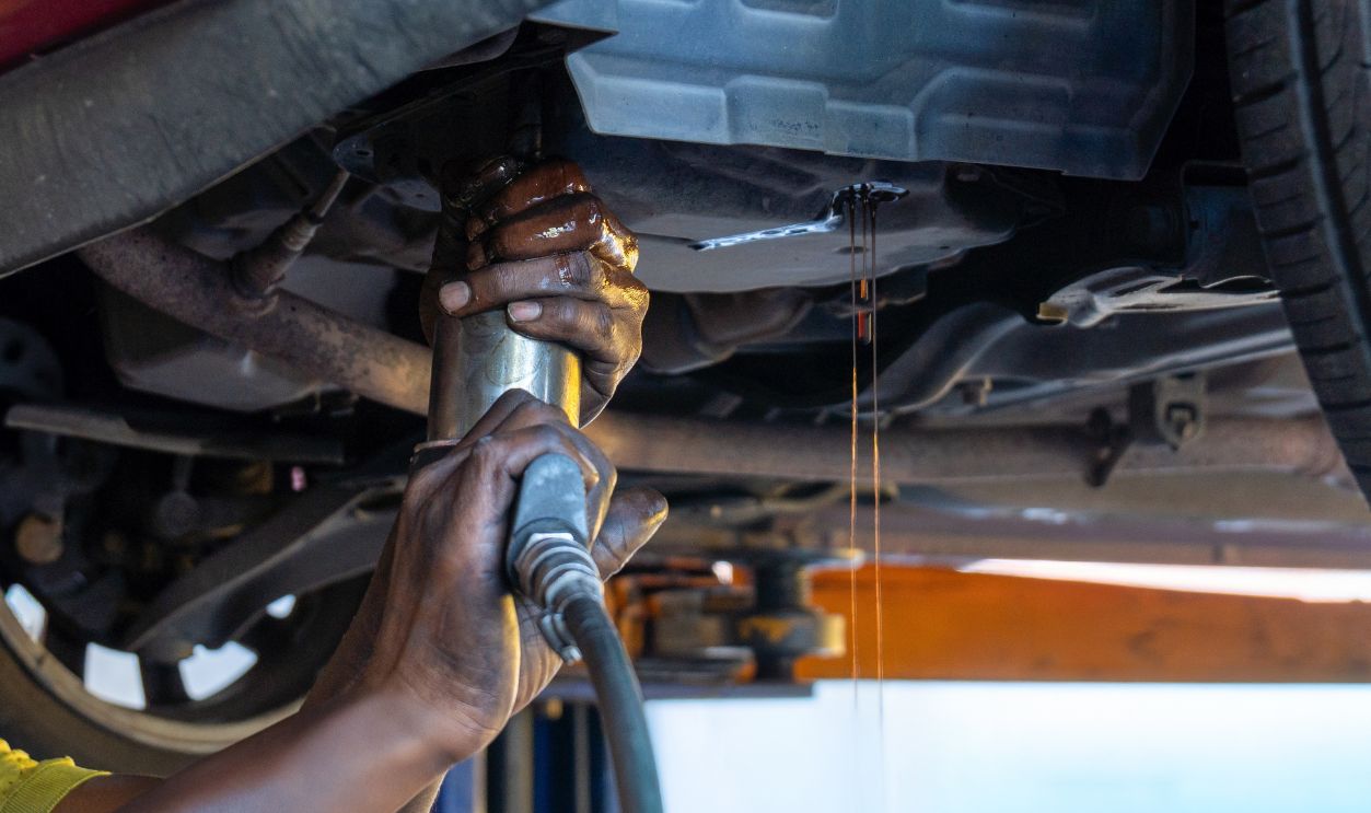 Auto mechanic draining transmission fluid from a vehicle during an ATF or Automatic Transmission Fluid oil change. Automotive maintenance, car repair and service concept.