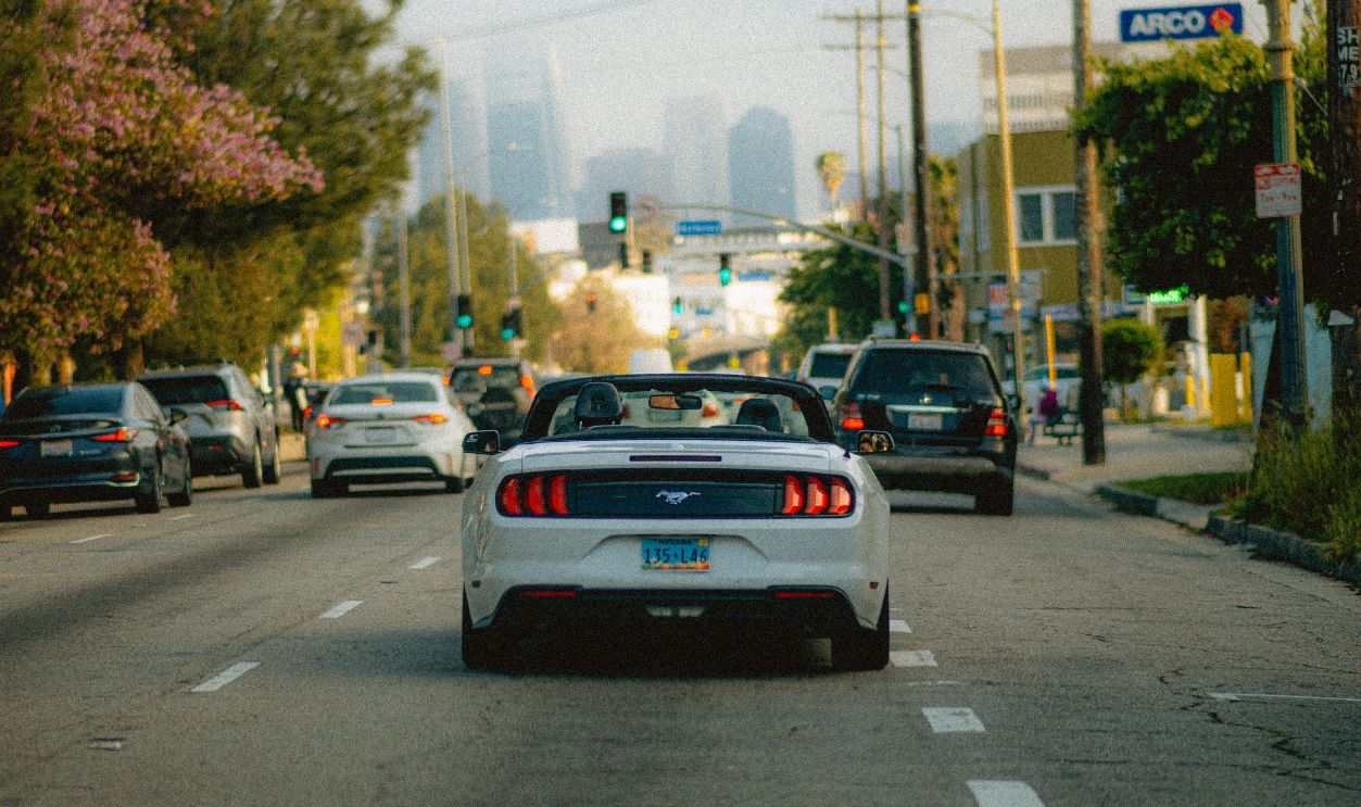 White convertible car on a busy Los Angeles street with a city skyline in the background.