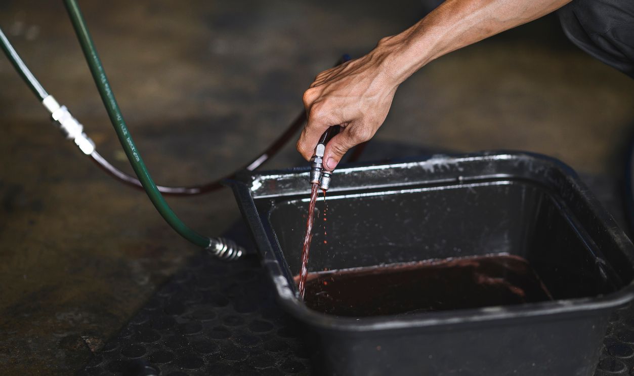Auto mechanic draining old used automatic transmission fluid into the oil drain pan.