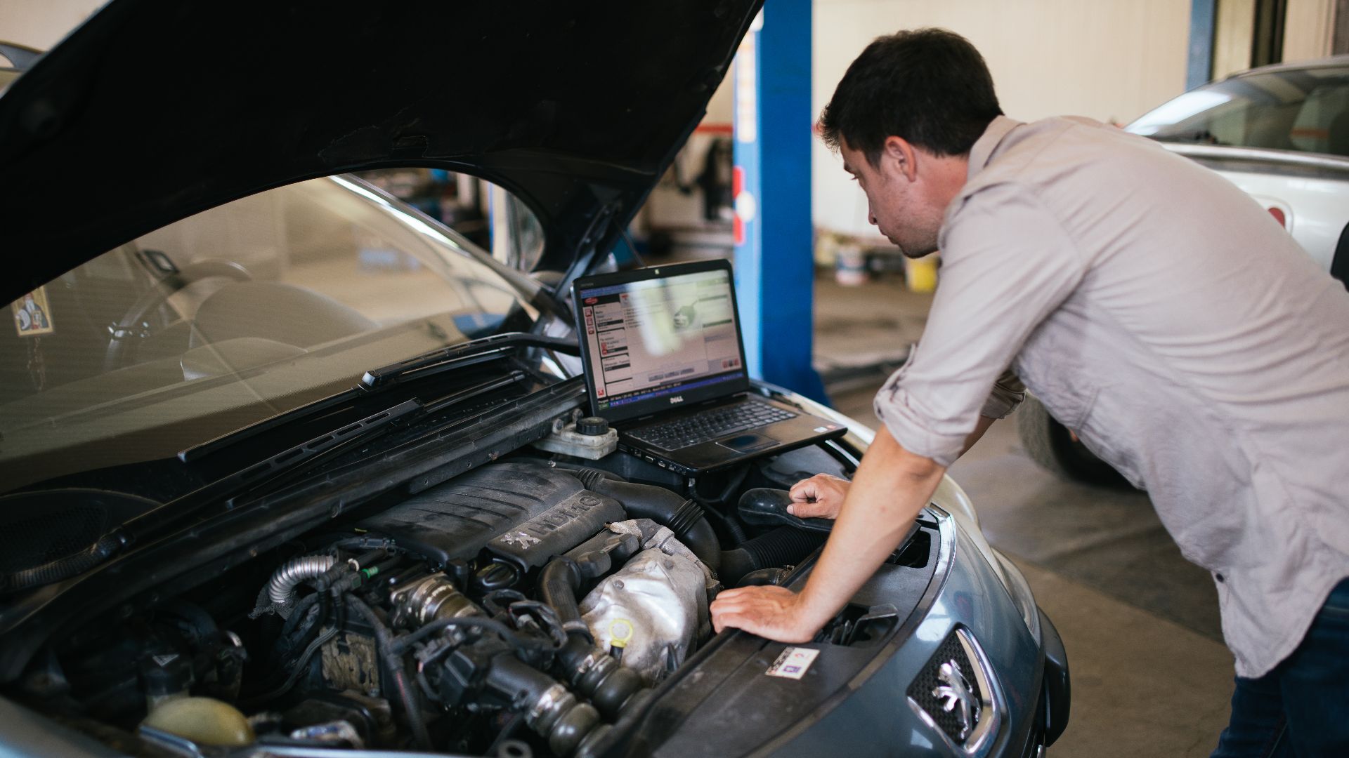 Young mechanic with laptop doing car diagnostic at automobile repair shop close