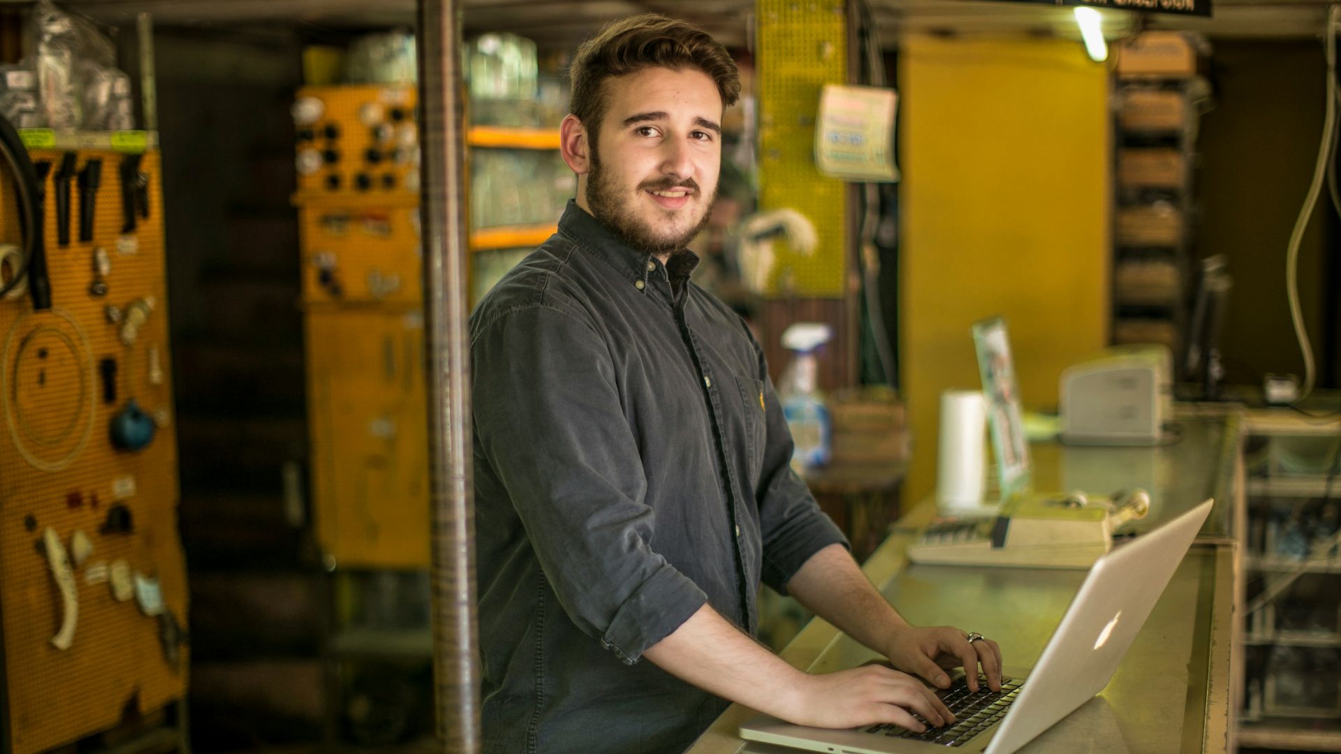 man standing and smiling while using MacBook