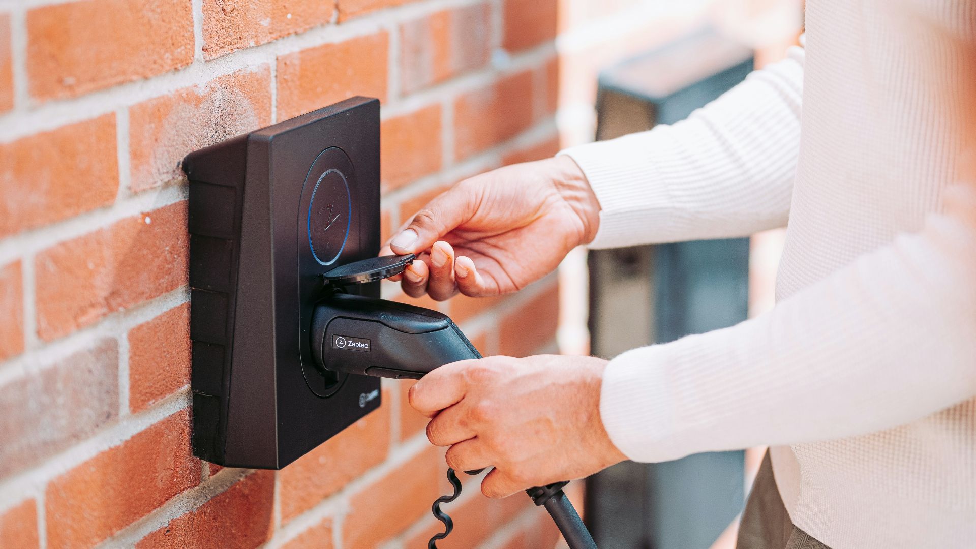 A woman is holding a phone and plugging it into a brick wall
