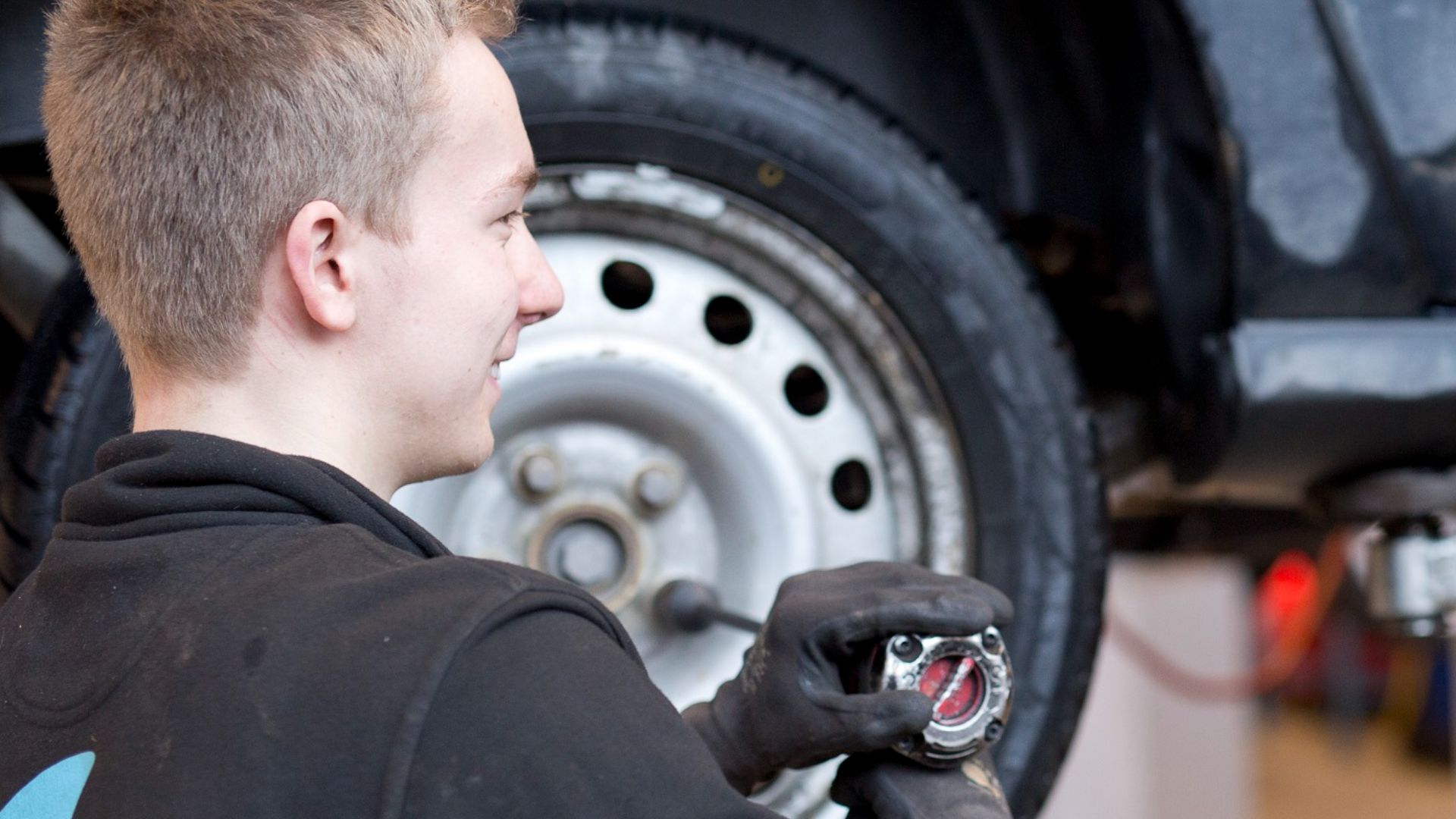 Mechanical student changing wheel on car at Kuben Upper Secondary School, Oslo Norway using a mechanical wrench.