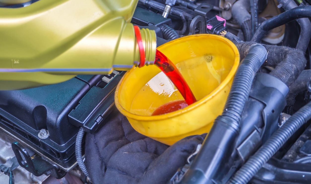 Transmission oil fill up in a car engine with yellow cone spire shape container.