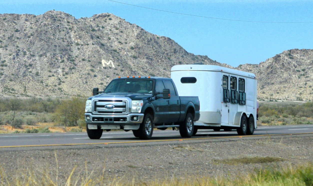Phoenix, Arizona - March 10 2026: A Ford full sized crew cab pickup tows a horse trailer along a rural desert highway.