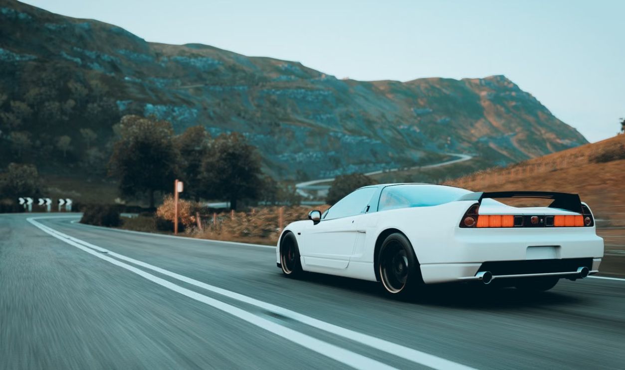 A sleek white sports car speeding through a scenic mountain road during the day