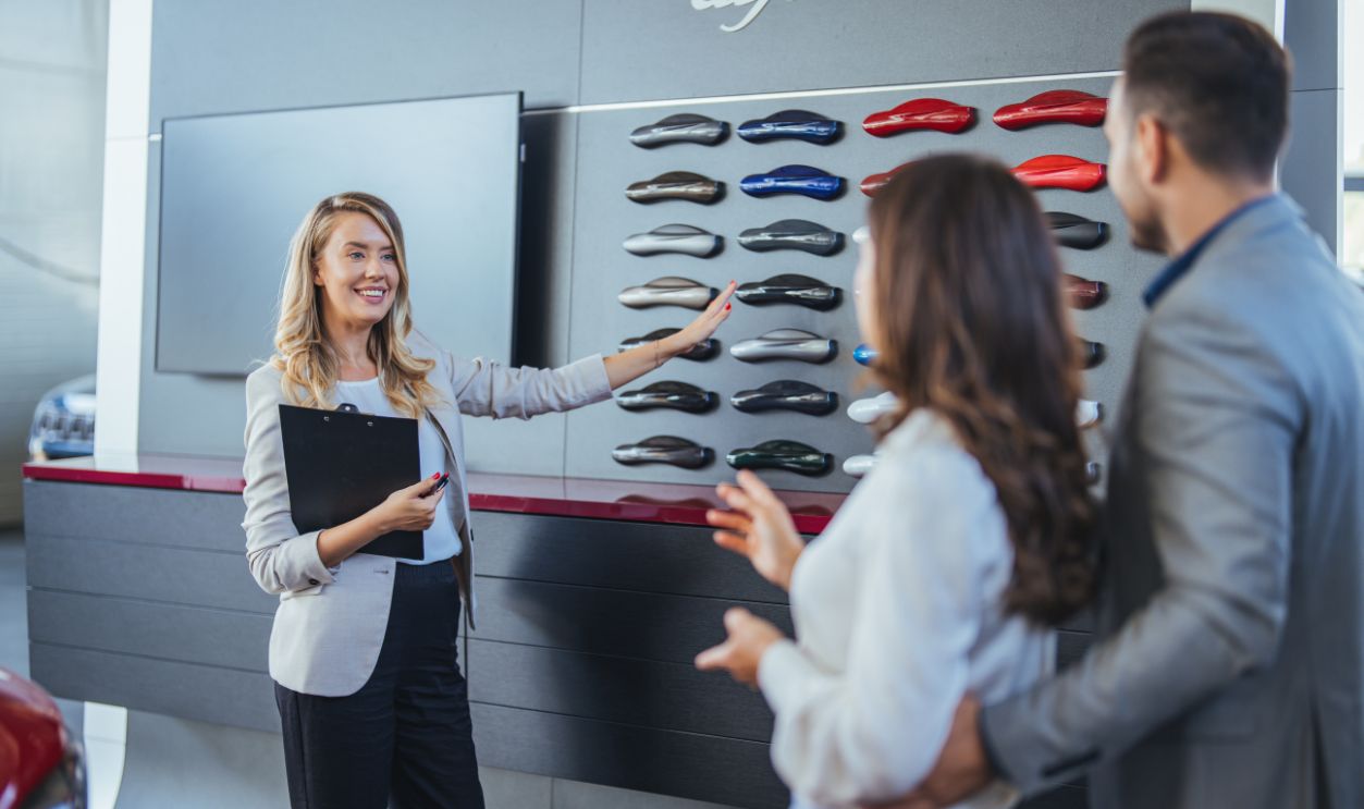 Salesperson offering help to a couple in choosing a right color for their new car in a car salon. Car sales business. Manager talking to couple, showing them new auto at dealership shop