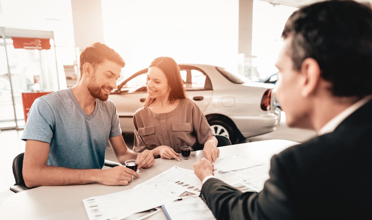 1175091667 : Happy Young Family Are Choosing A New Car In Showroom. Dialogue With Dealer. Cheerful Customer. Automobile Salon. Make A Decision. Cup Of Coffee. End Of A Deal. Good Offer. Buyer And Seller.