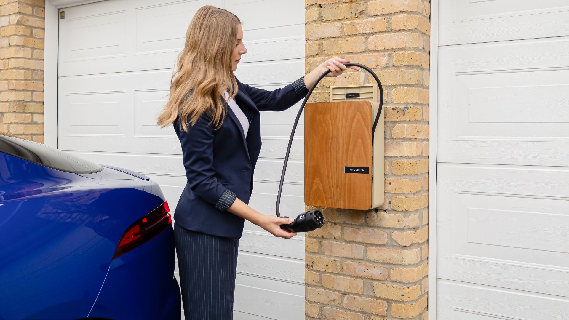 A woman using a home electric vehicle charger on a brick wall in a garage.