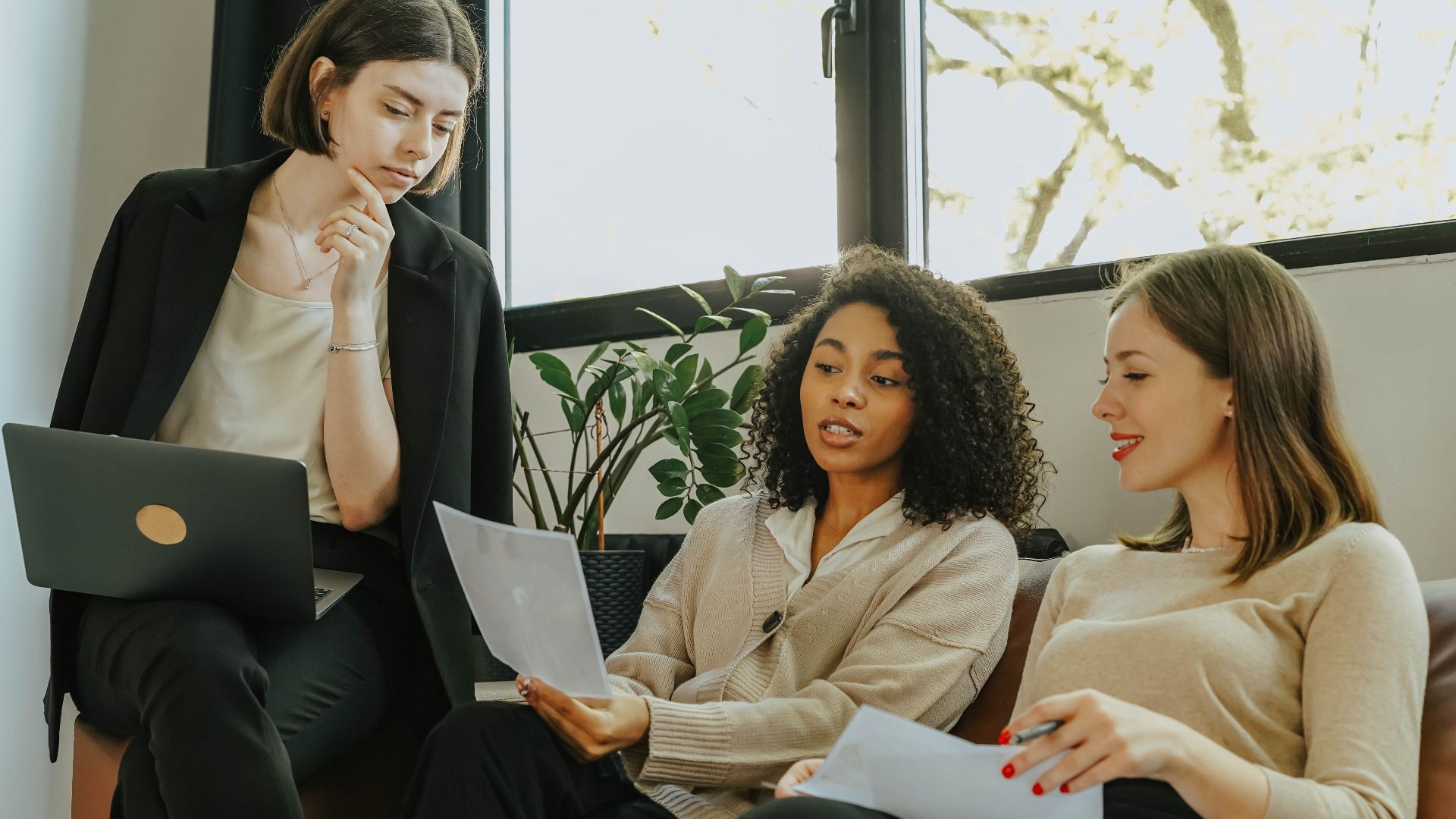 Three professional women engaged in a collaborative meeting in a modern office setting.