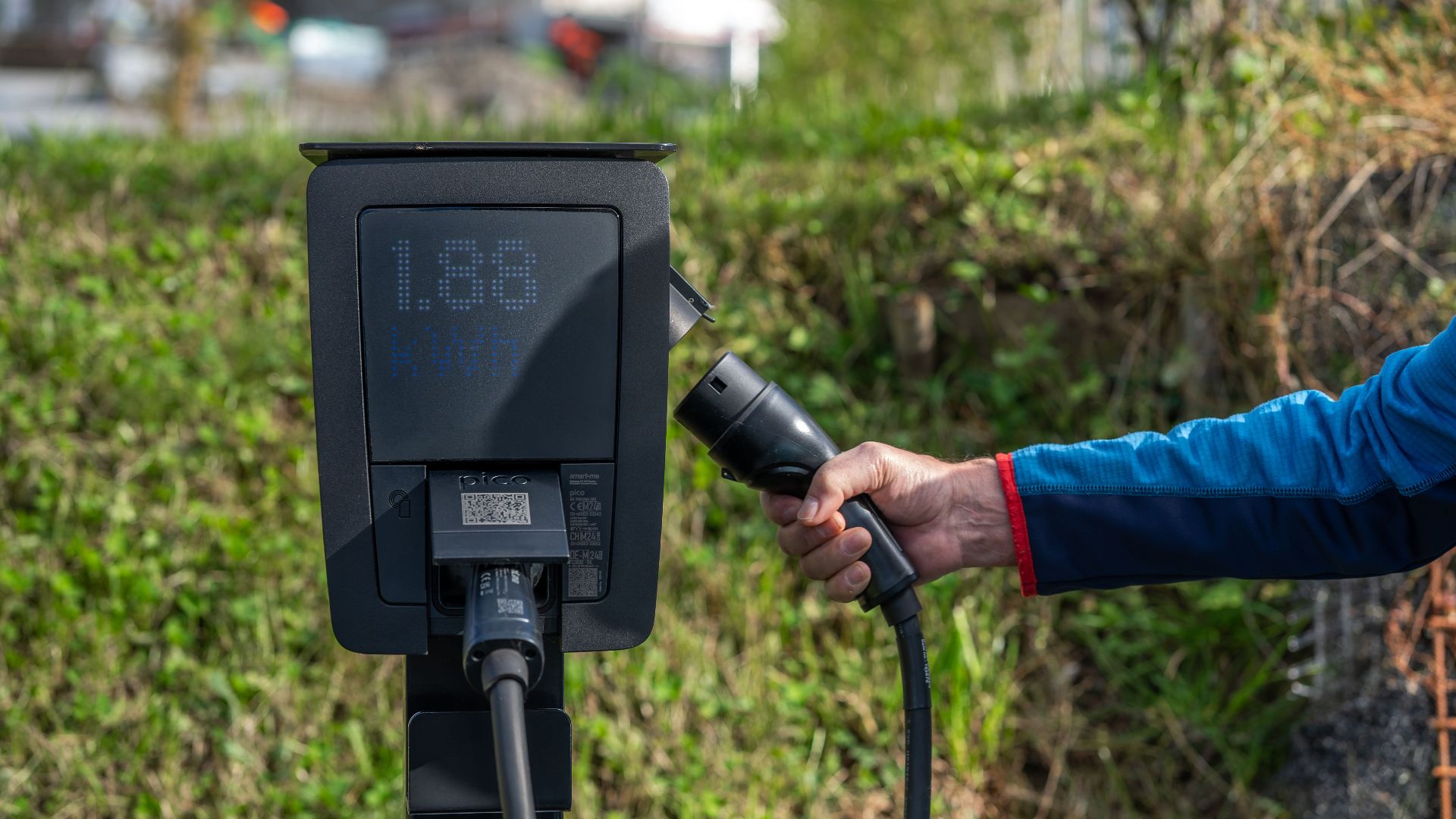 An outdoor electric car charging station with a hand holding a charging cable.